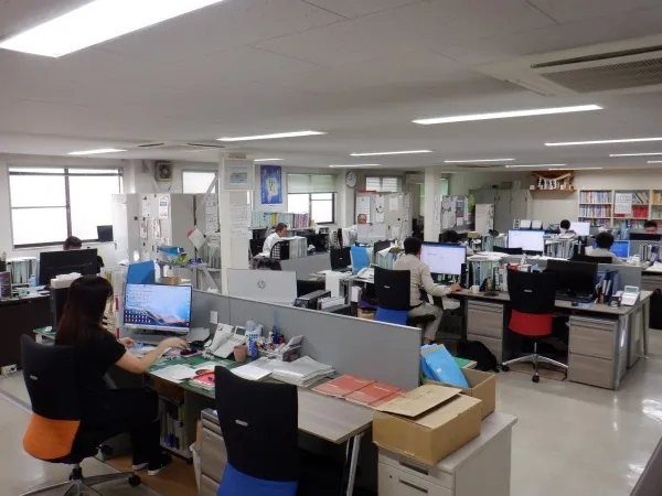 計電工業の事務所内。複数のデスクにパソコンが並び、社員が作業している様子