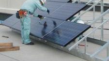 ビルの屋上で、作業員が太陽電池パネルを架台に据え付けている様子